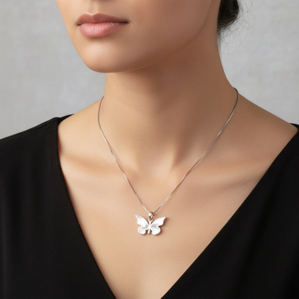 Silver butterfly pendant necklace on a pink surface with a wooden border