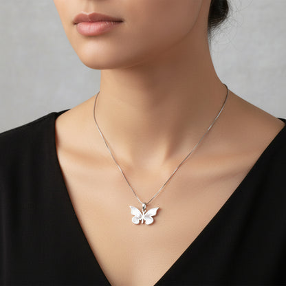 Silver butterfly pendant necklace on a pink surface with a wooden border